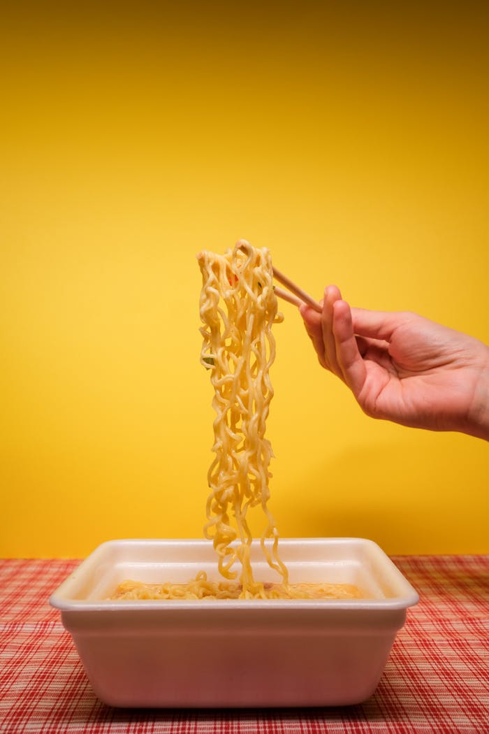 Crop anonymous person using bamboo chopsticks while eating traditional instant noodles prepared in container in kitchen